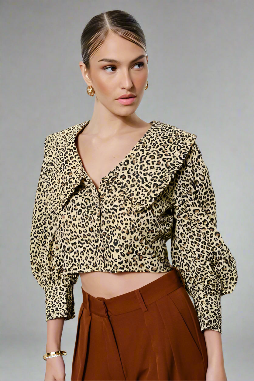 Woman wearing a leopard print blouse and brown pants against a white background