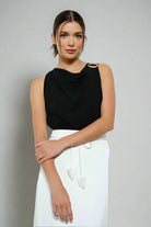 Woman wearing a black sleeveless top and  white pants against a white background